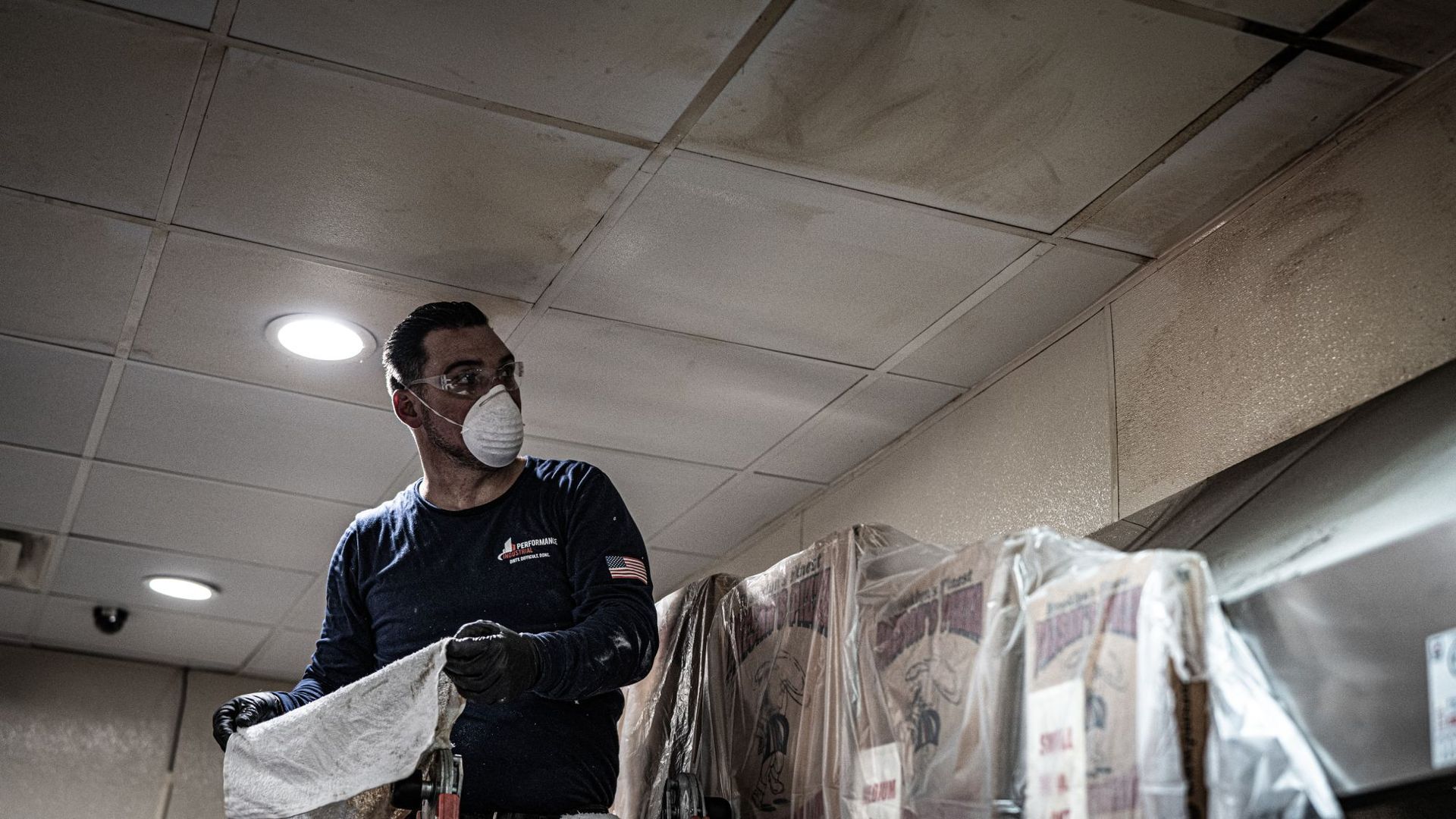 A man wearing a mask is cleaning a ceiling in a kitchen.