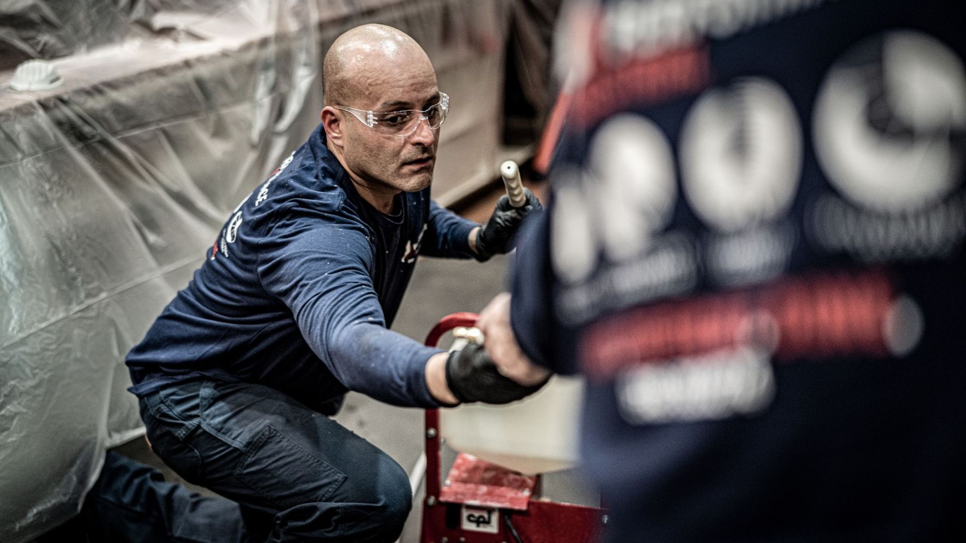 A man is kneeling down in a warehouse while working on a machine.