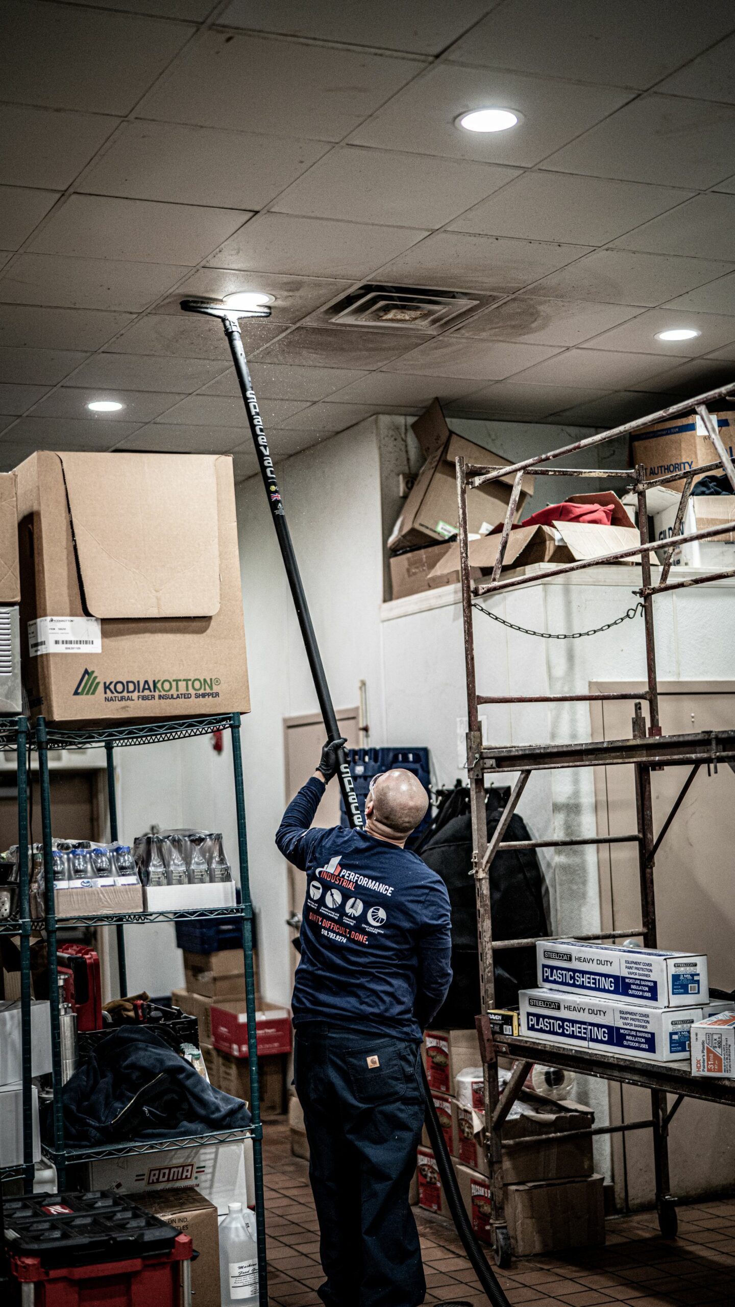 A man is cleaning the ceiling of a room with a vacuum cleaner.