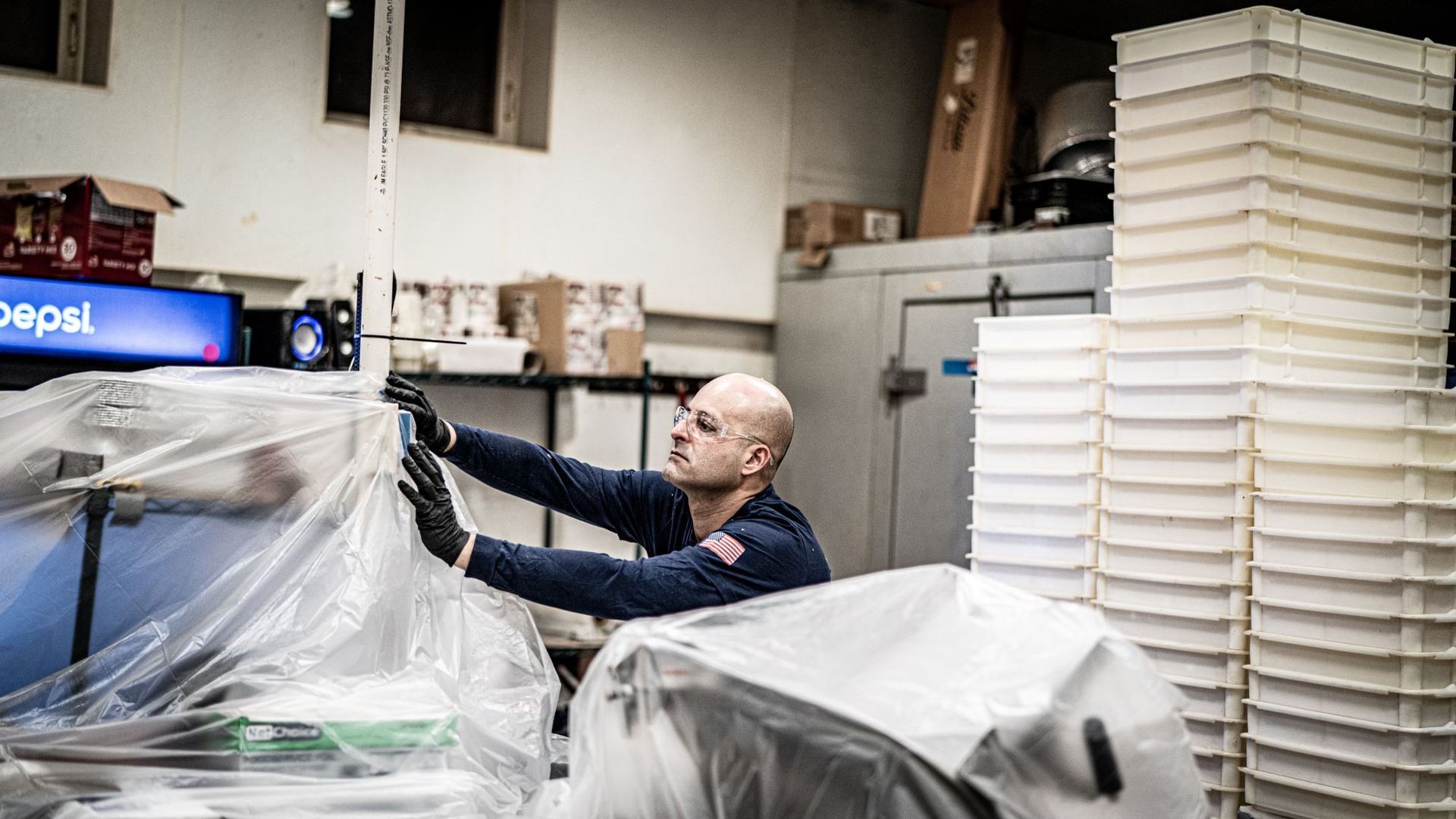 A man is covering a machine with plastic wrap in a kitchen.