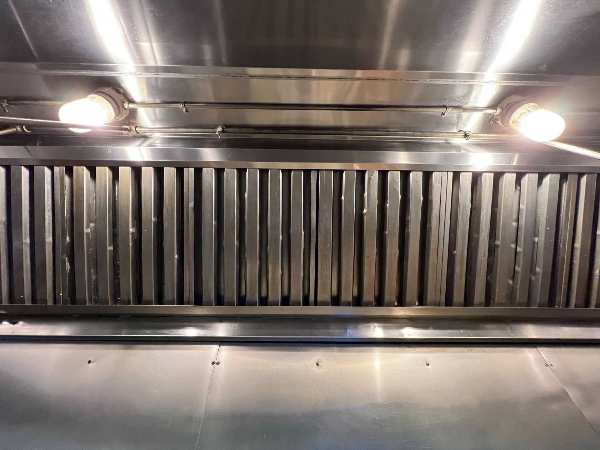 A stainless steel exhaust hood with lights on it in a kitchen.