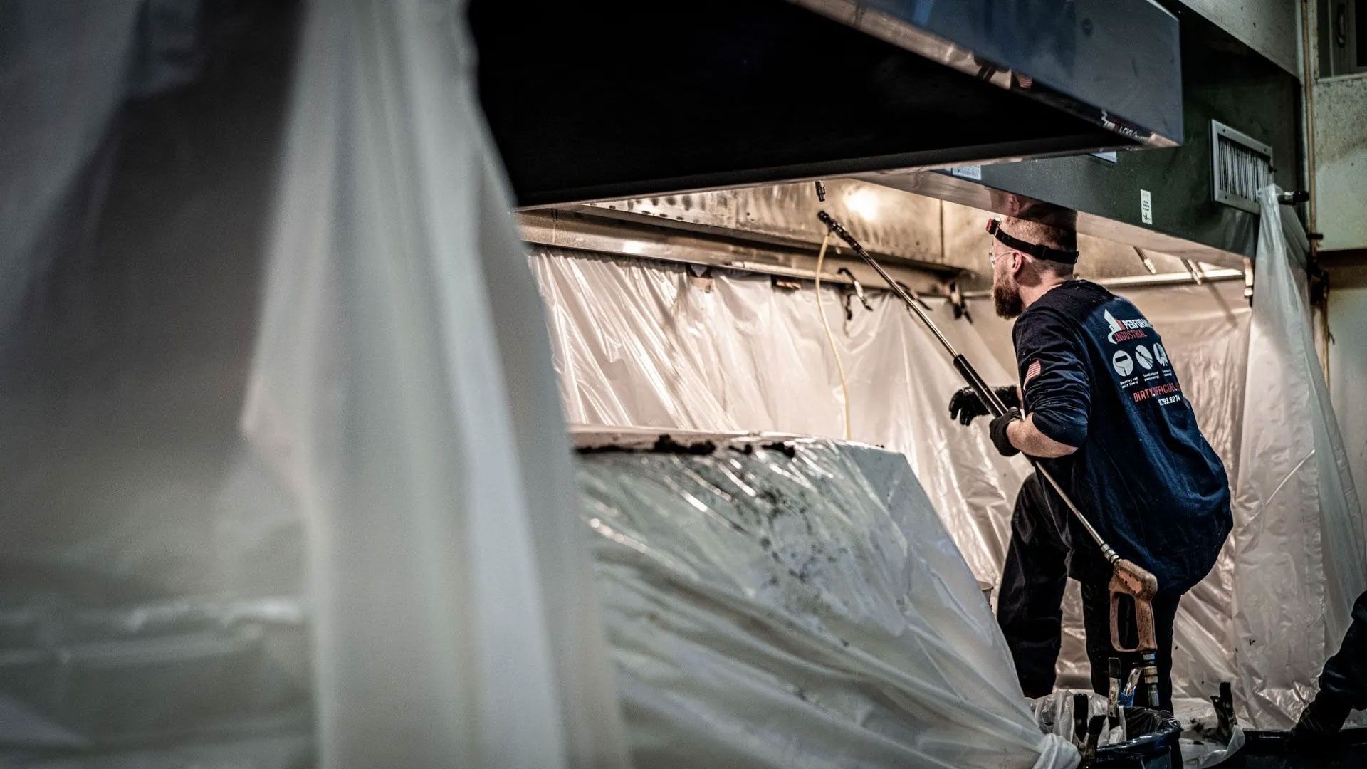 Worker cleaning equipment under a large hood with plastic sheeting. Worker cleaning equipment under a large hood with plastic sheeting.