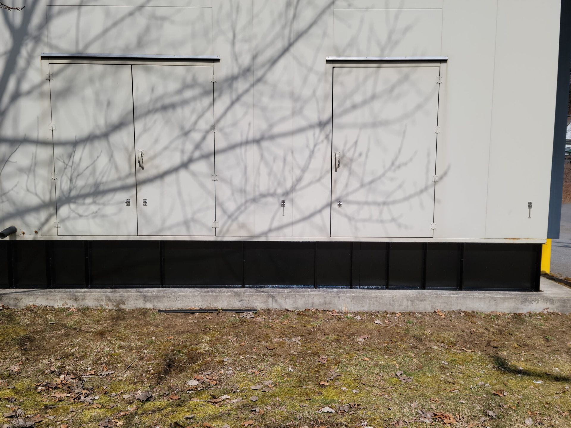 A white building with black trim and a shadow of a tree on the side of it.