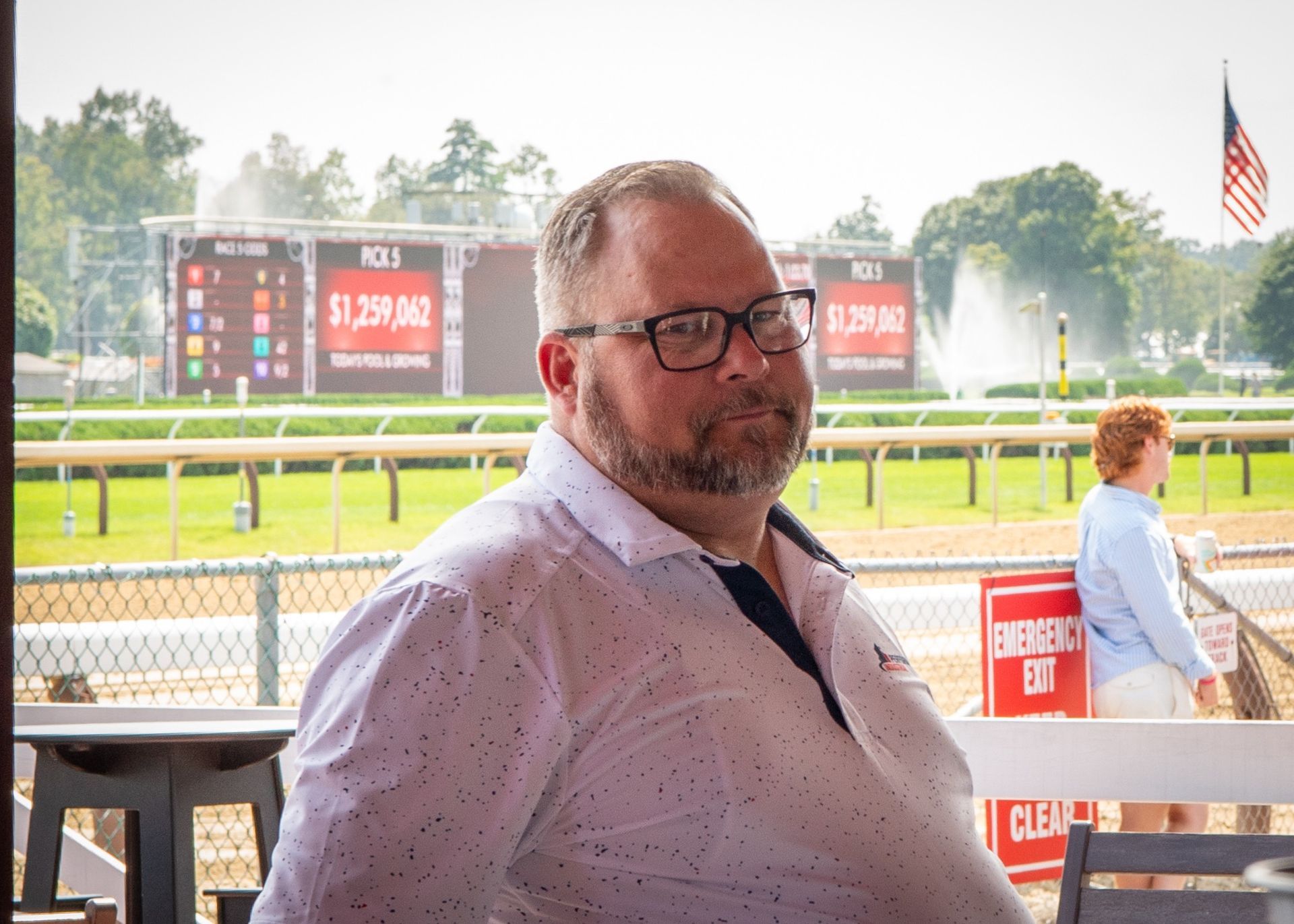 A man wearing glasses is sitting in front of a race track.