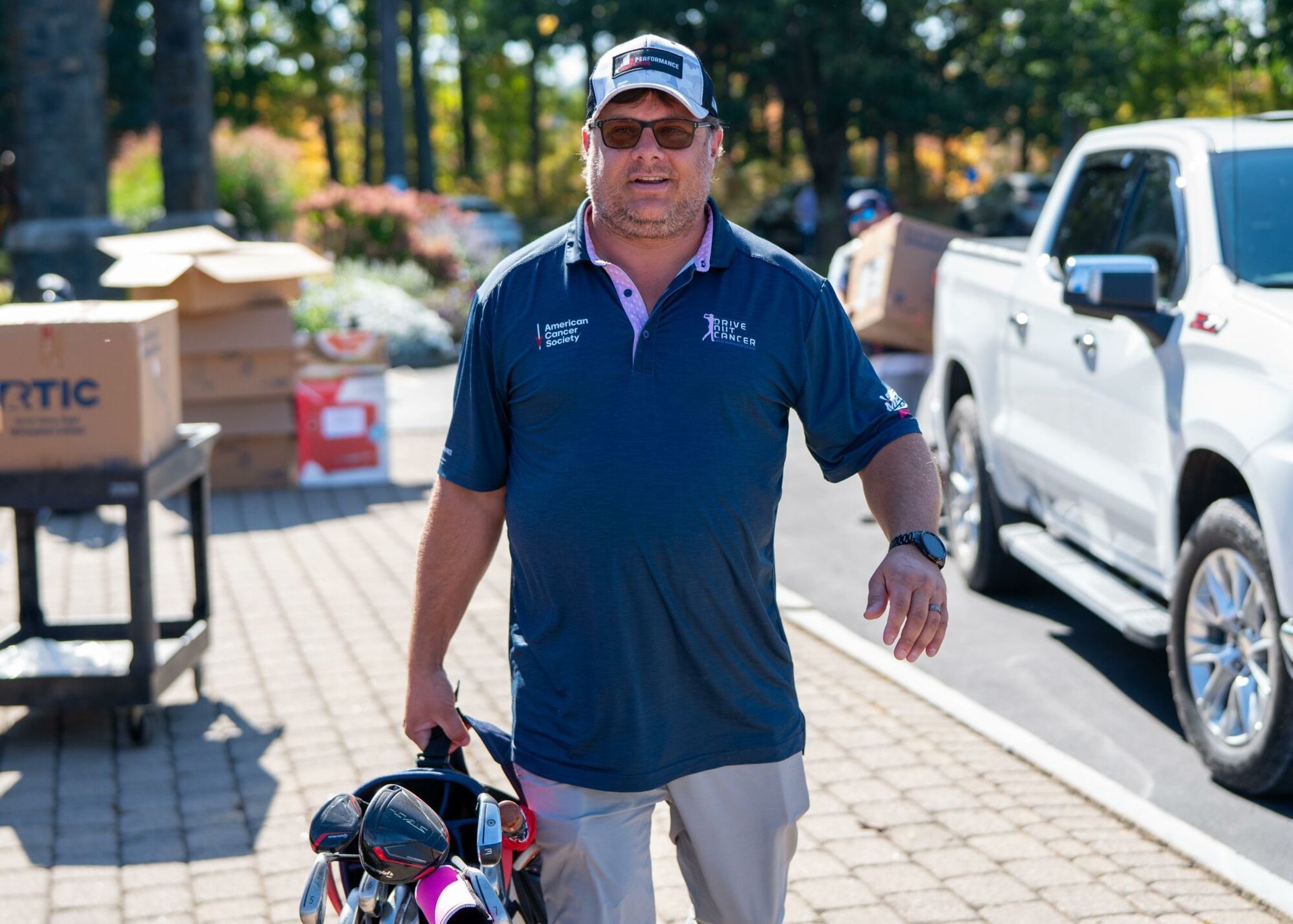 A man is walking down a sidewalk holding a golf bag.