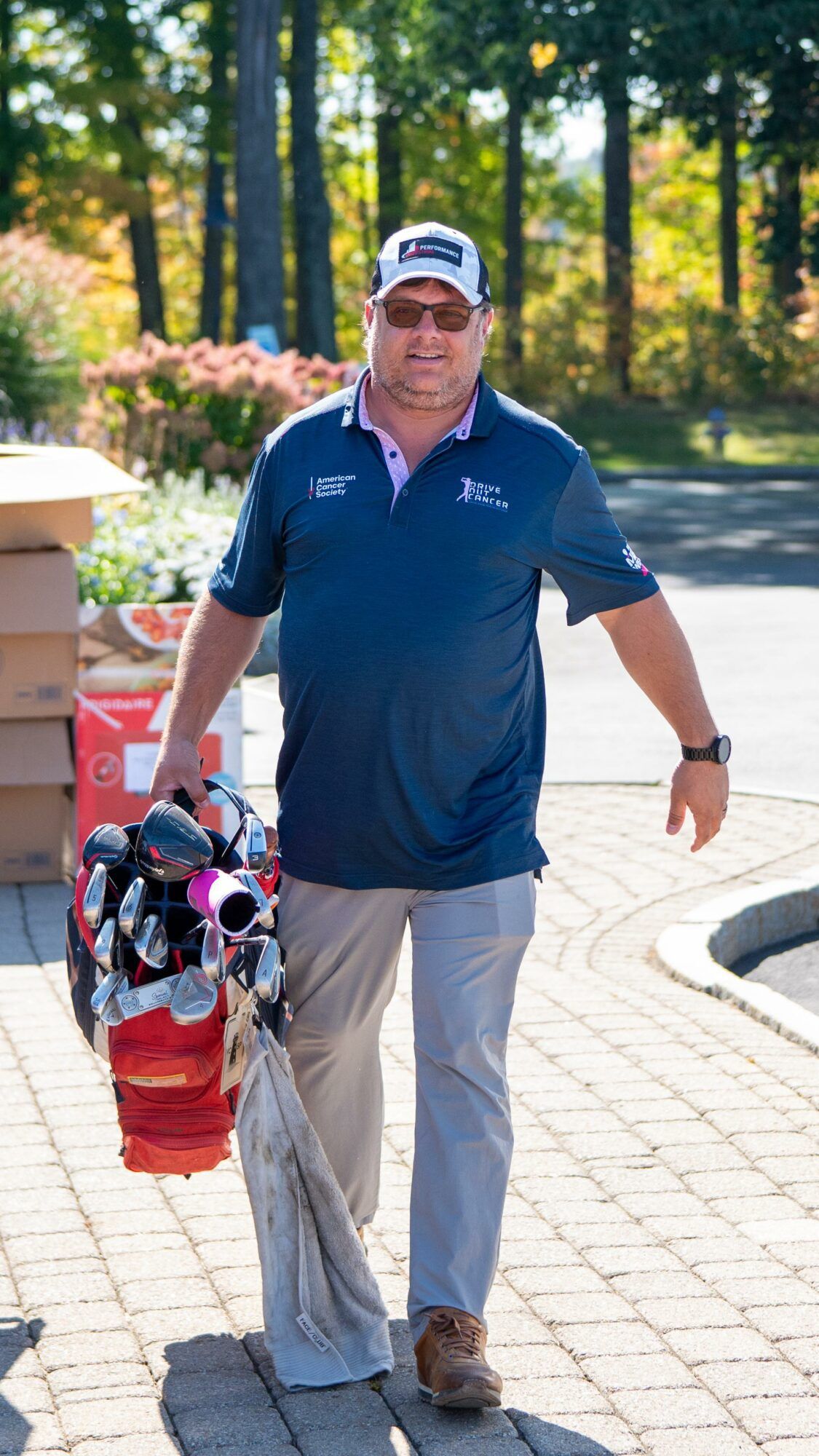 A man is carrying a golf bag on a brick sidewalk.