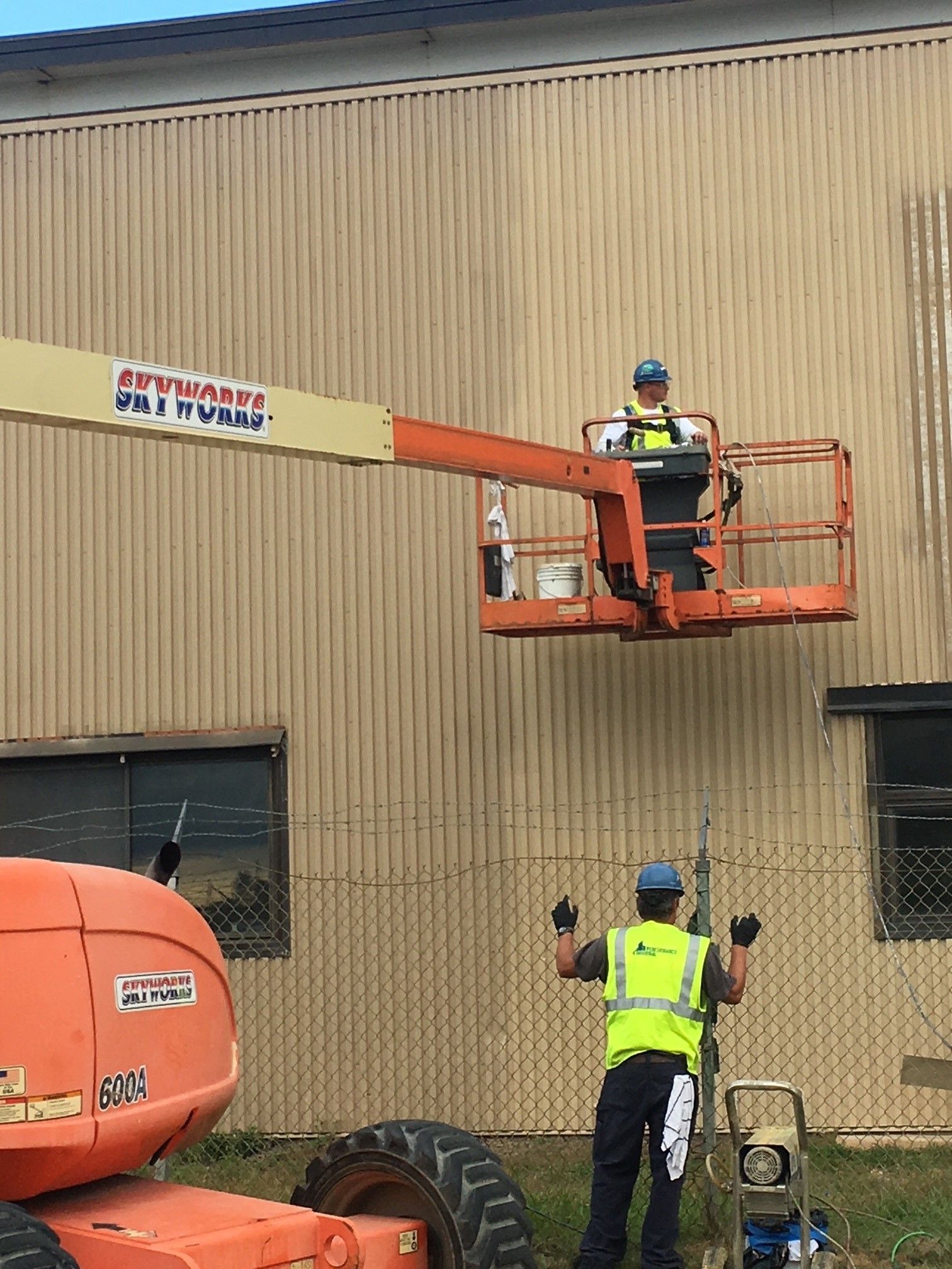 A man is standing in front of a building while a man is sitting on a lift.
