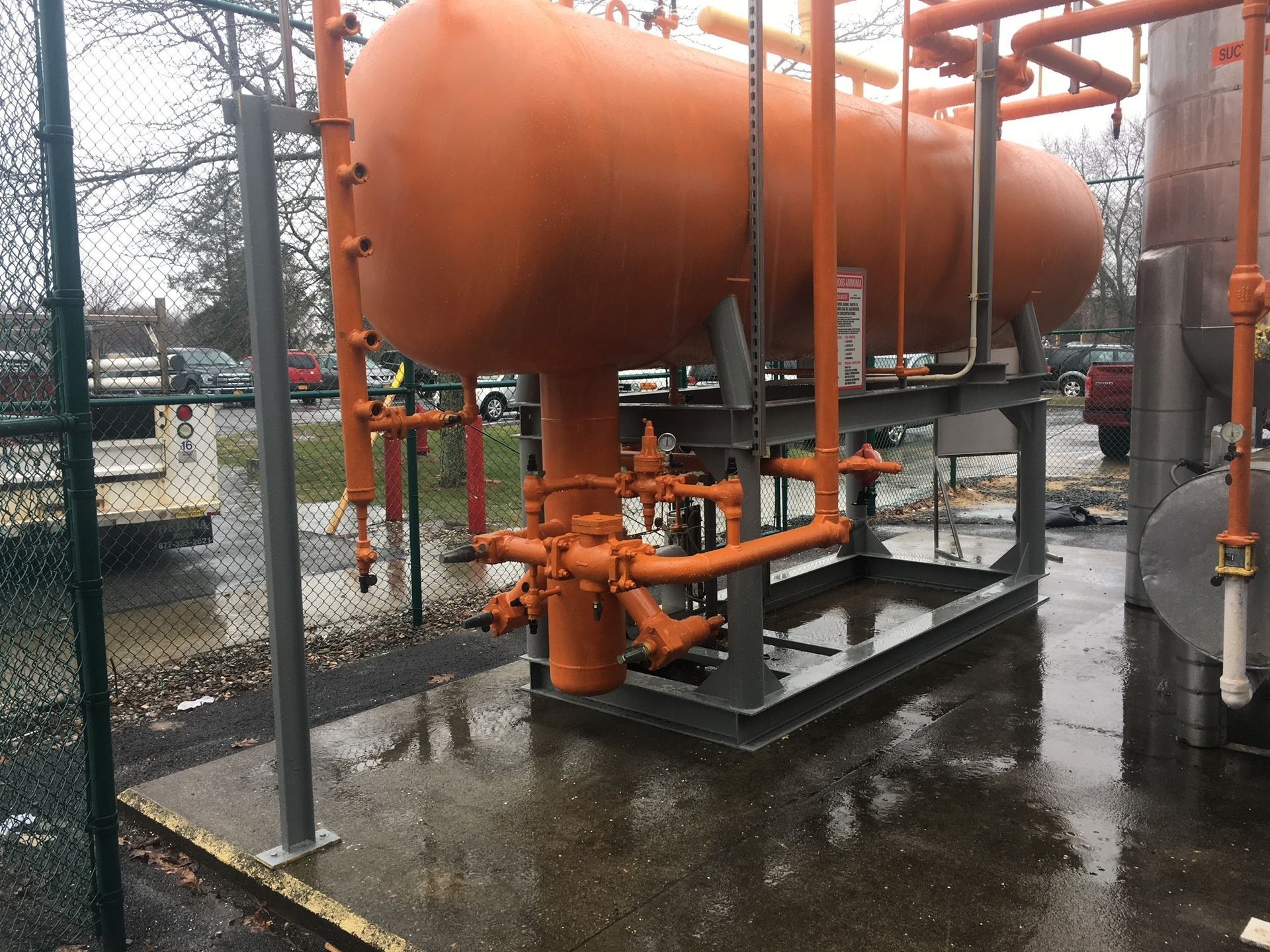 A large orange tank is sitting in a parking lot next to a chain link fence.