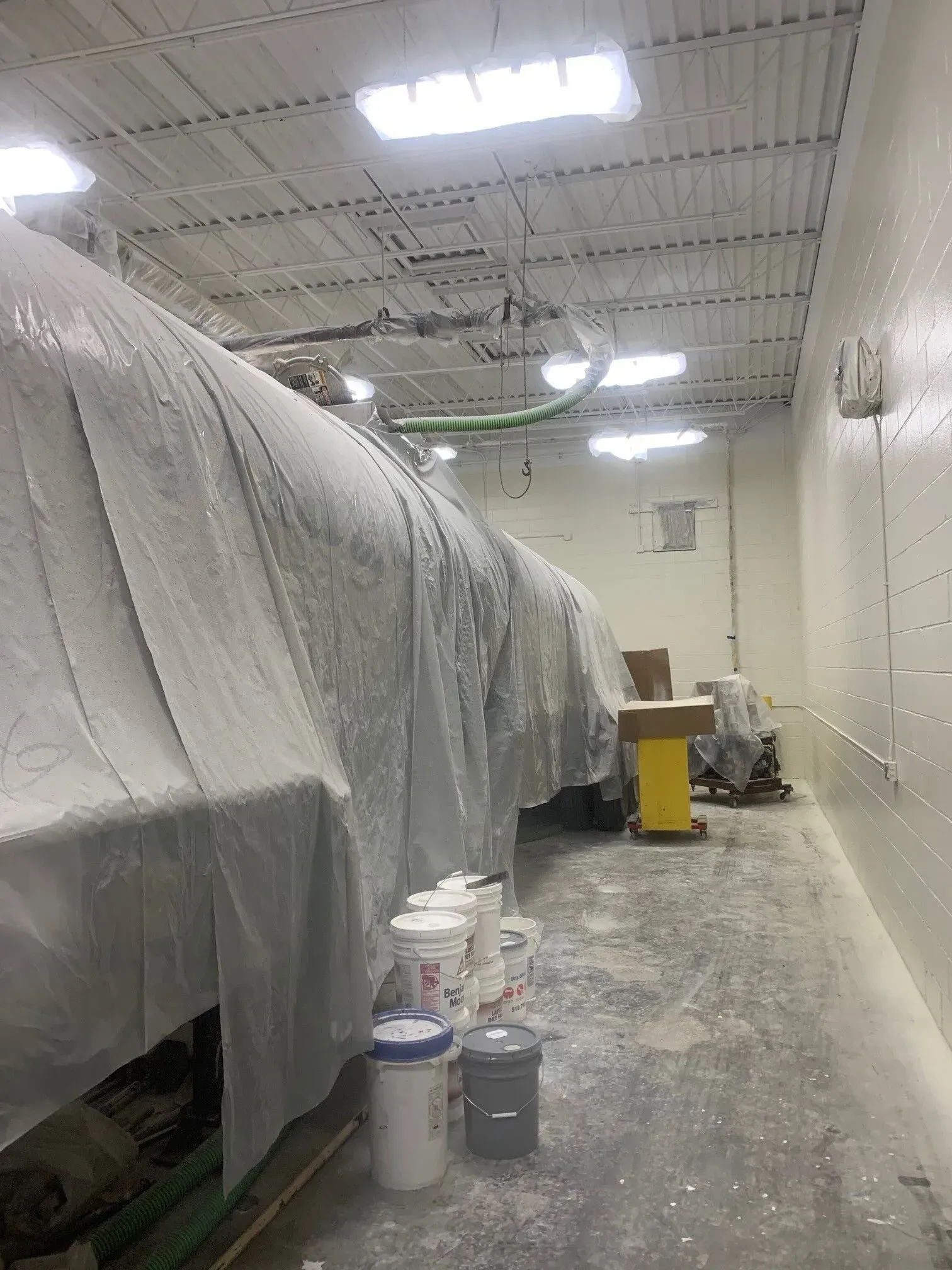 A room with a lot of buckets on the floor and a large object covered in plastic.