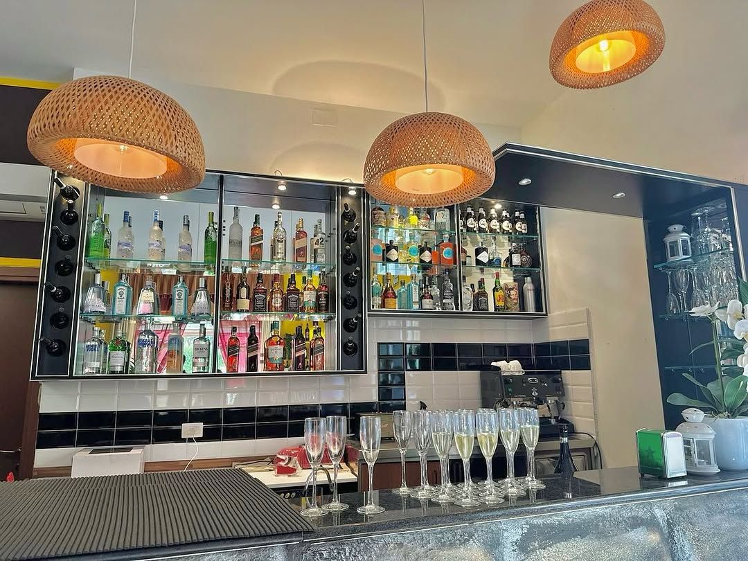 Bar con lampade a sospensione in vimini, scaffali pieni di liquori e bicchieri da champagne.