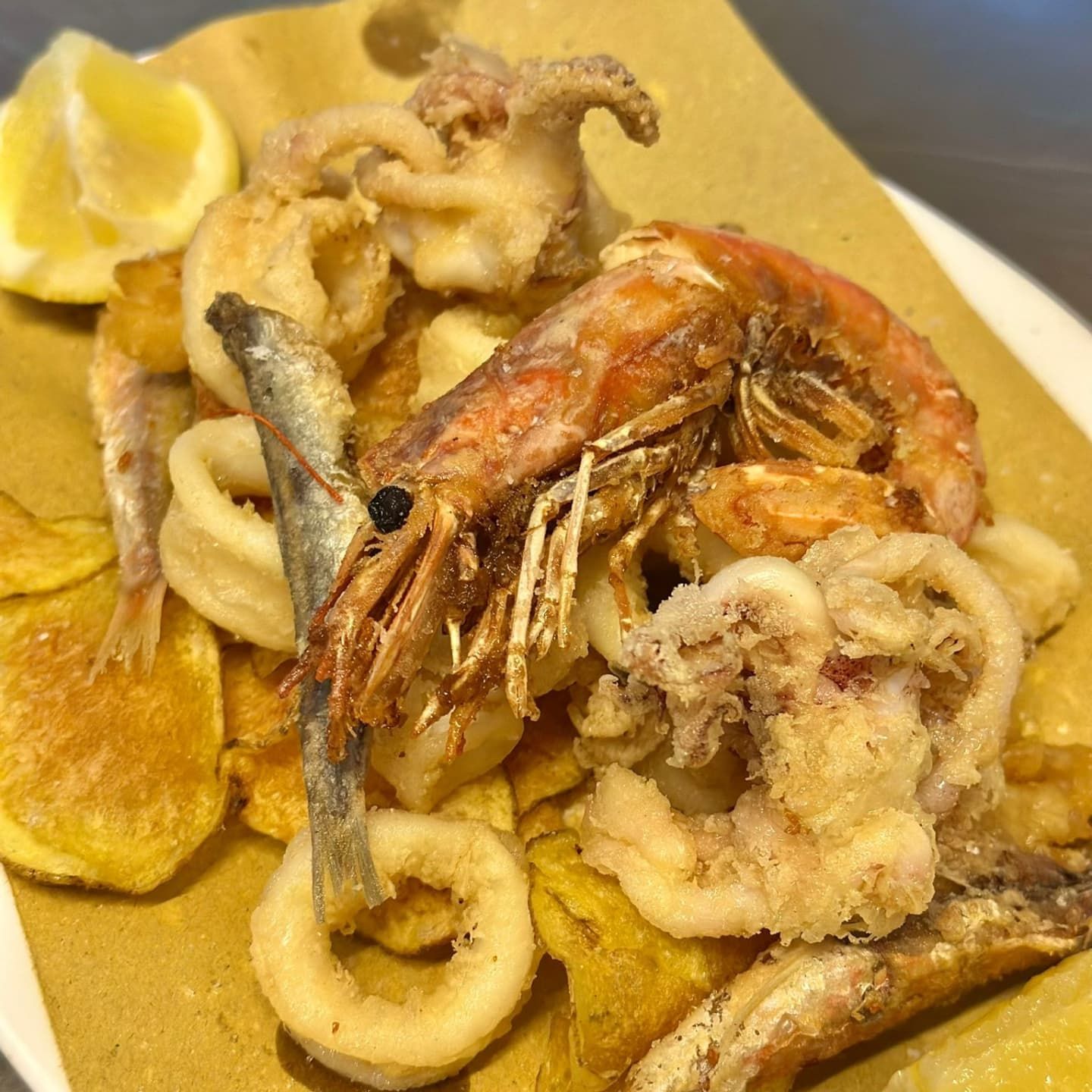 Piatto di pesce fritto con gamberi, calamari, pesce e patatine fritte, servito con limone.
