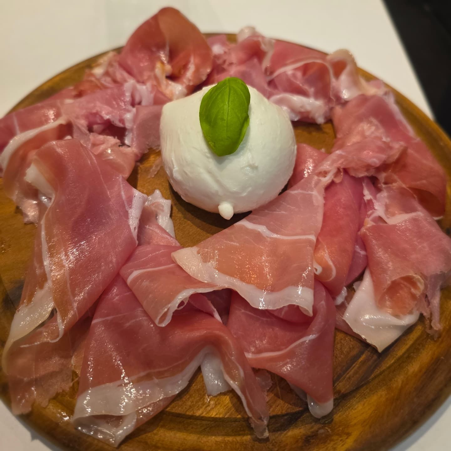 Antipasto di prosciutto e mozzarella su un tagliere di legno, guarnito con basilico.