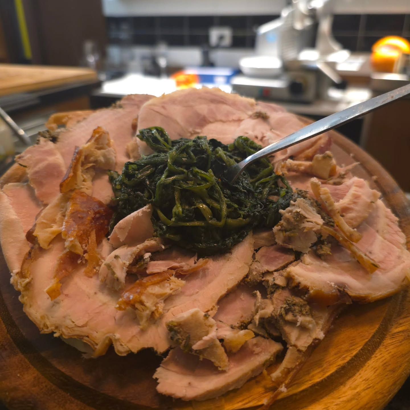Arrosto di maiale a fette con contorno di verdure verdi su un vassoio di legno. Una forchetta è nelle verdure.