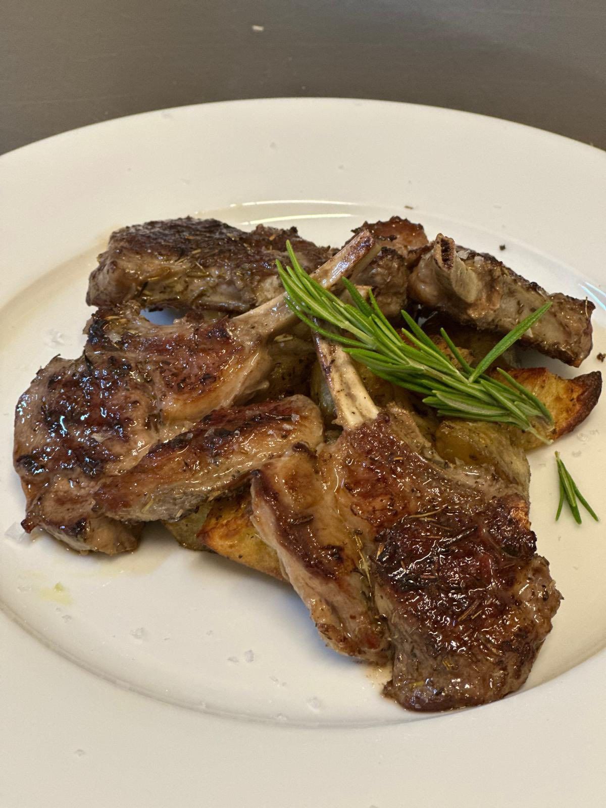 Costolette di agnello alla griglia con rametto di rosmarino su un piatto bianco.