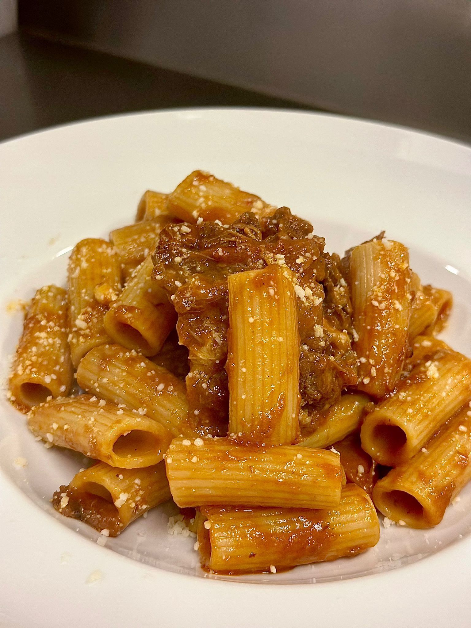 Piatto di pasta: rigatoni al ragù, guarniti con parmigiano grattugiato, su un piatto bianco.