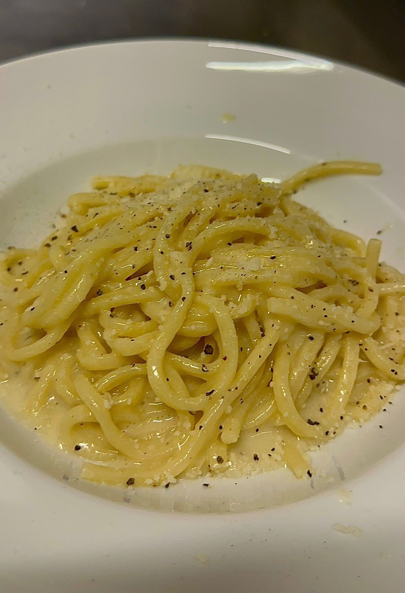Spaghetti alla carbonara in una ciotola bianca, conditi con salsa e spolverati con pepe nero.