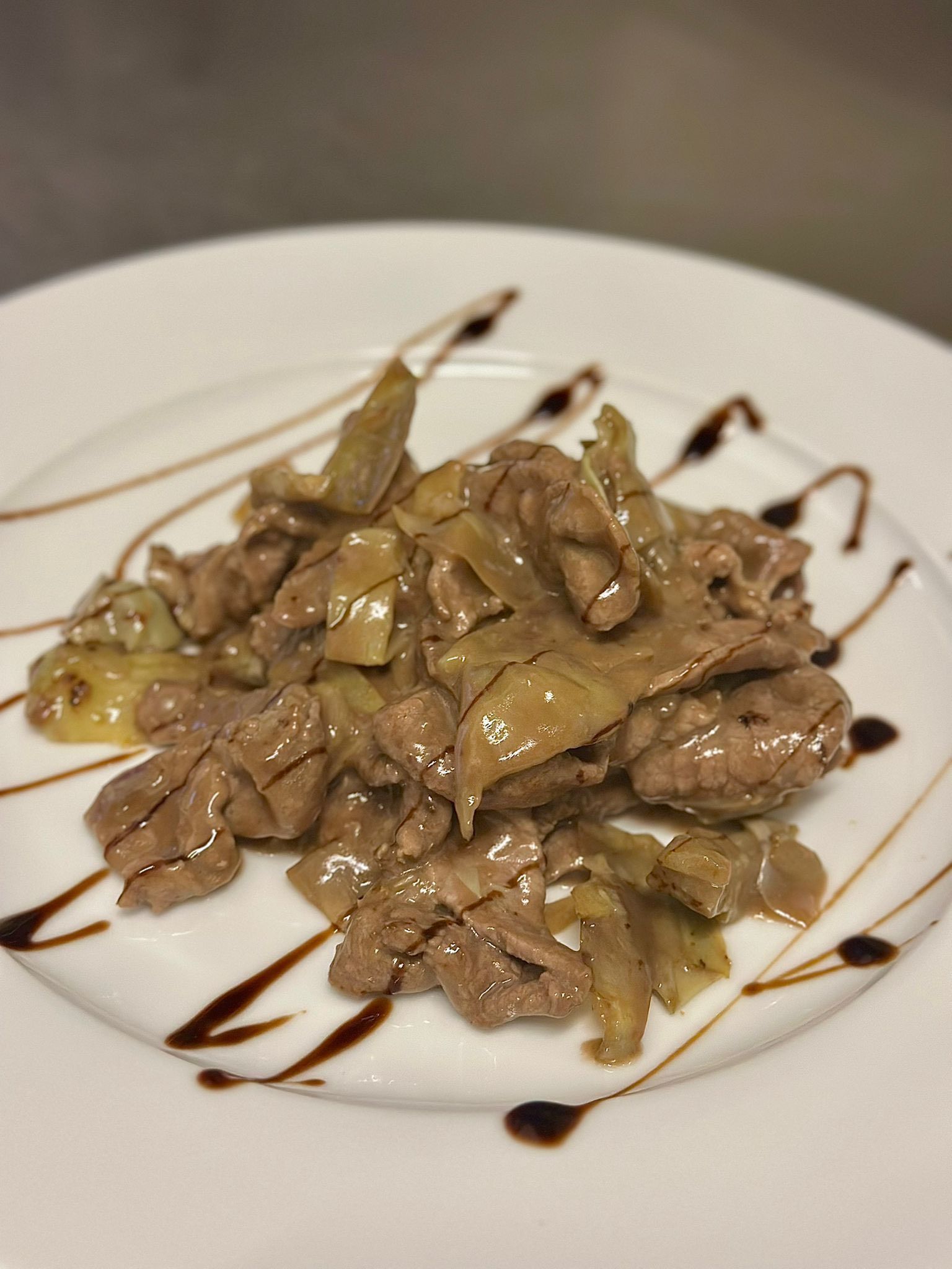 Manzo saltato e carciofi su un piatto bianco, conditi con glassa balsamica.