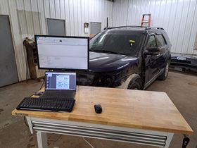 A laptop computer is sitting on a wooden table next to a car.