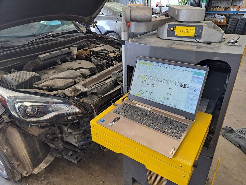 A laptop is sitting on a yellow table next to a car with the hood open.
