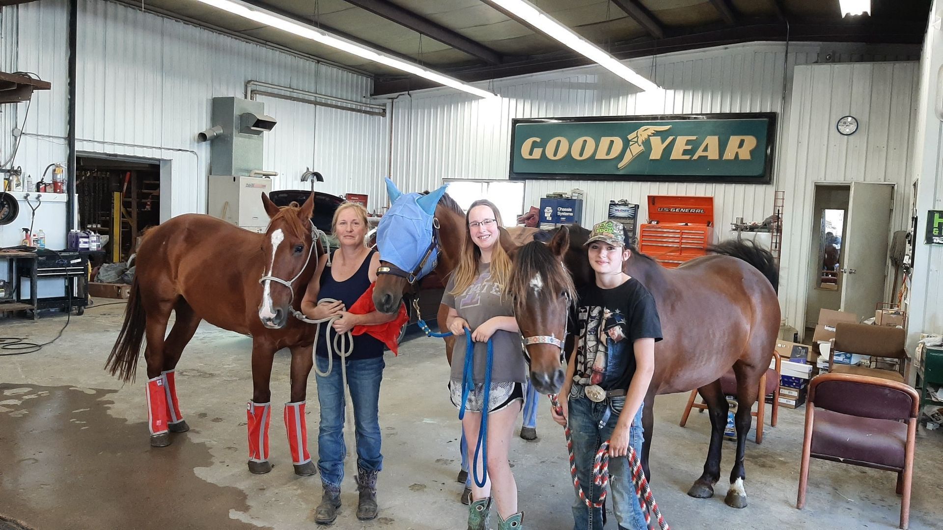 A group of people standing next to horses in a garage.