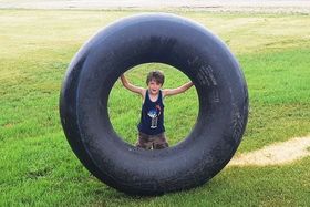 A young boy is standing inside of a large tire.