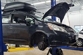 A car is sitting on a lift in a garage with the hood open.
