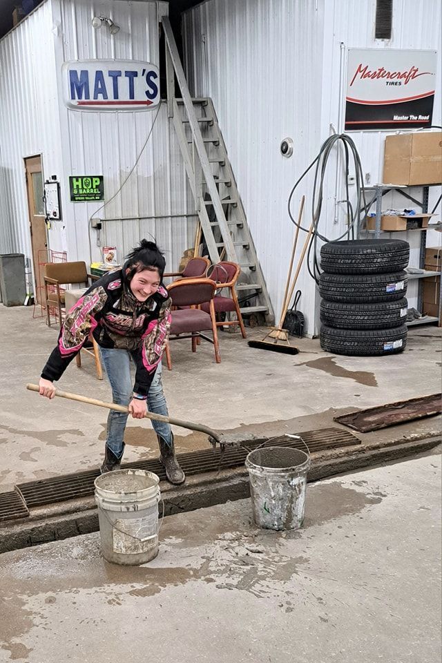 A woman is holding a shovel in front of a garage.