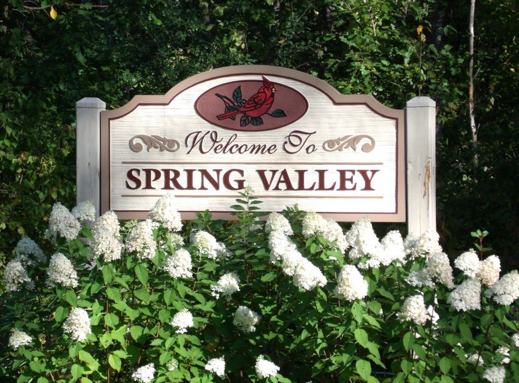 A welcome to spring valley sign is surrounded by white flowers