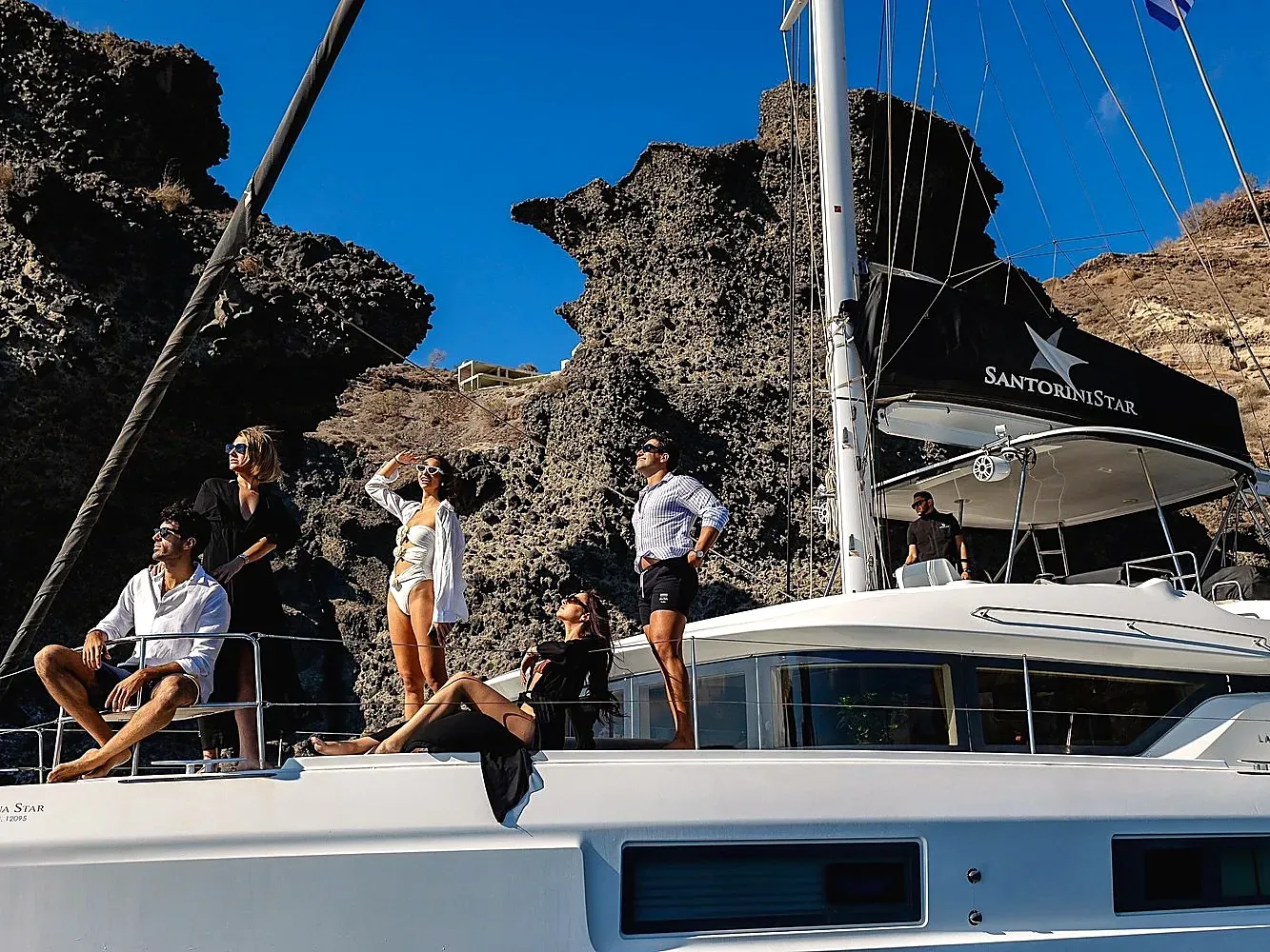 Guests on a private Santorini catamaran cruise sailing past volcanic cliffs as part of a land and sea combo tour