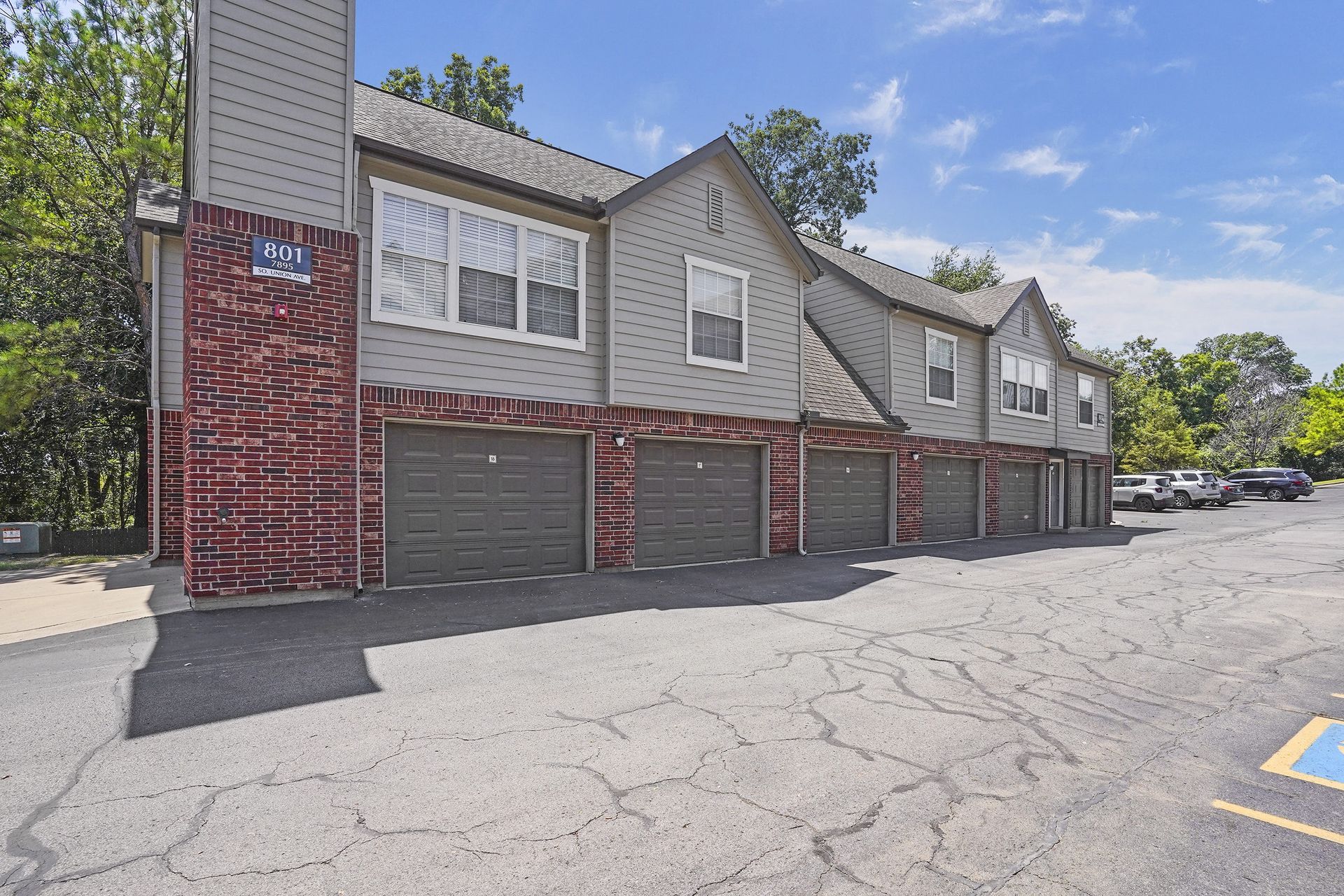 Apartment building with garage doors, red brick accents, and parking lot on a sunny day.