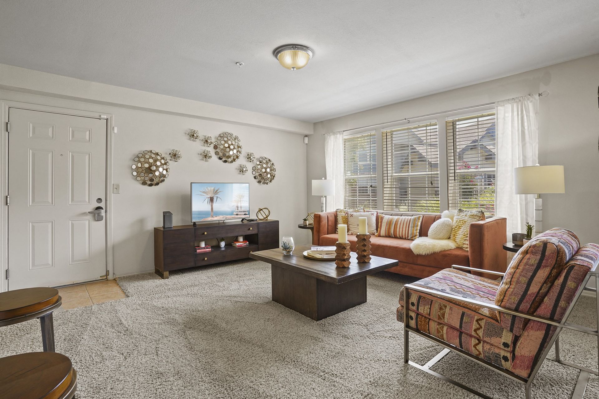 Living room in an apartment with a sofa, an accent chair, coffee table, TV, and large front window.