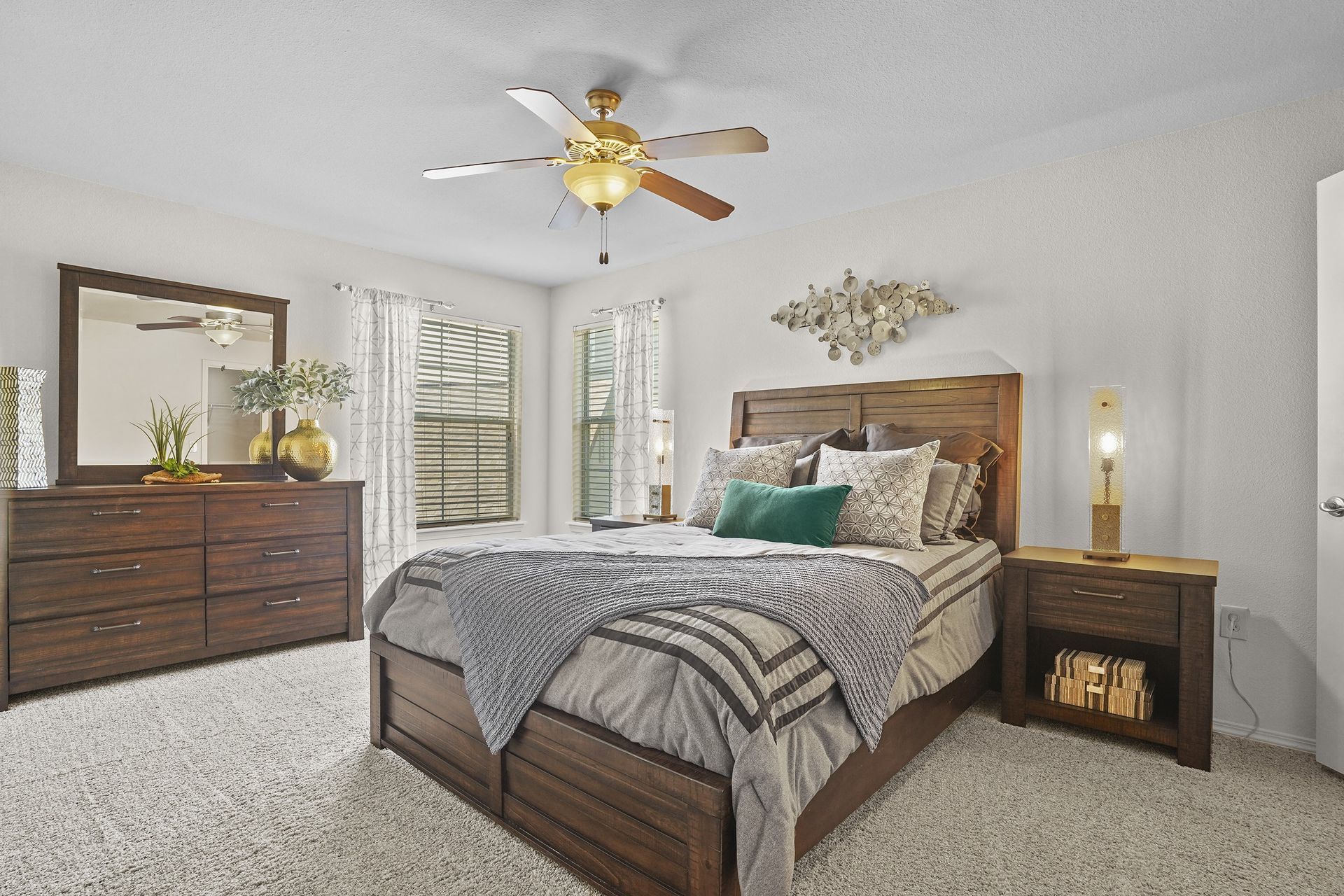 Bedroom in apartment with dark wood bed, dresser with mirror, nightstands, and ceiling fan.