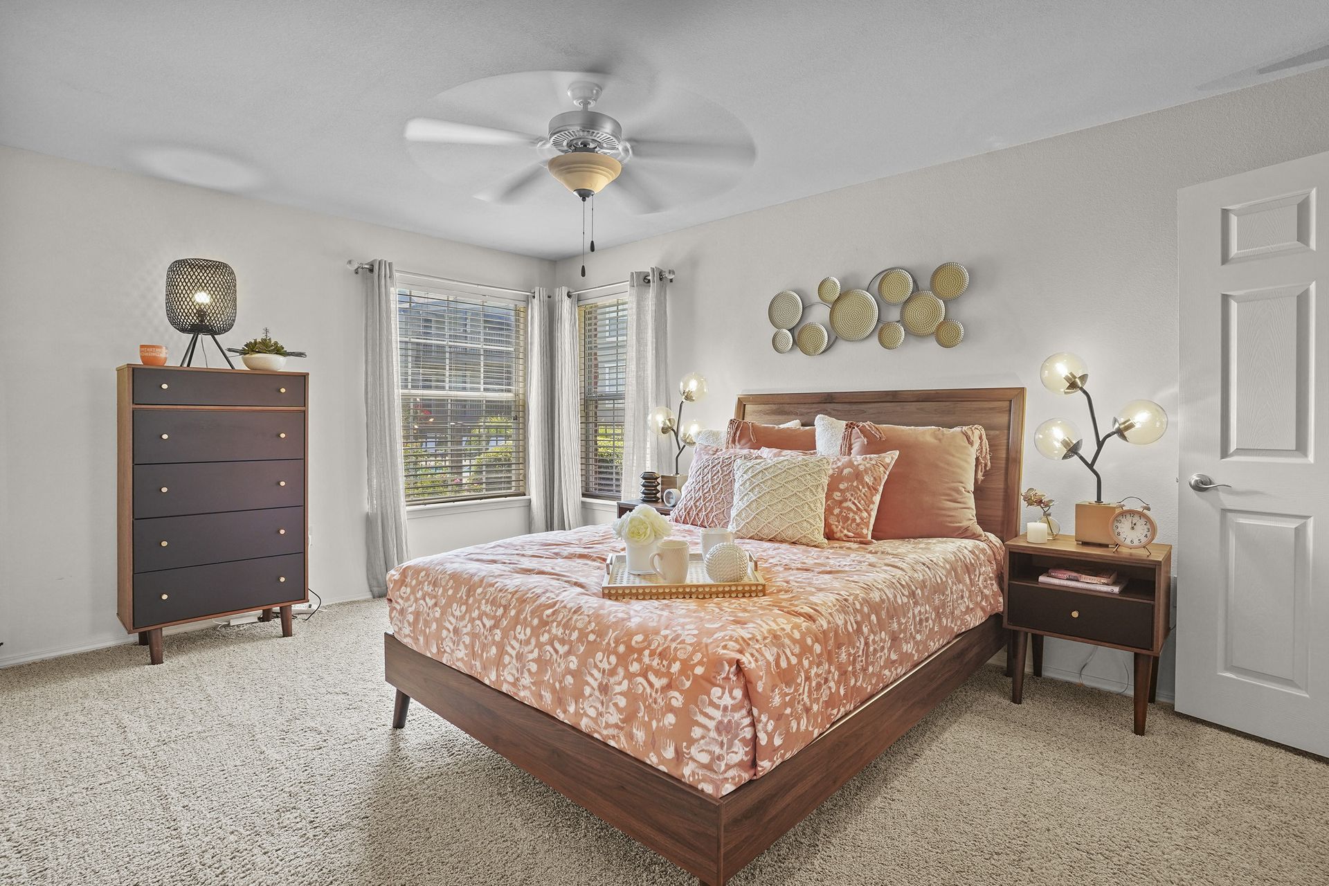 Bedroom in an apartment with a wooden bed, dresser, two nightstands, and large windows.