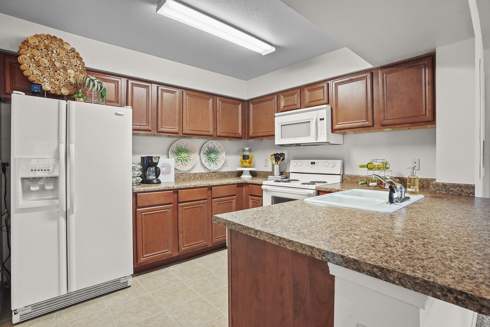 Kitchen in an apartment with brown cabinets, white appliances, and an island.