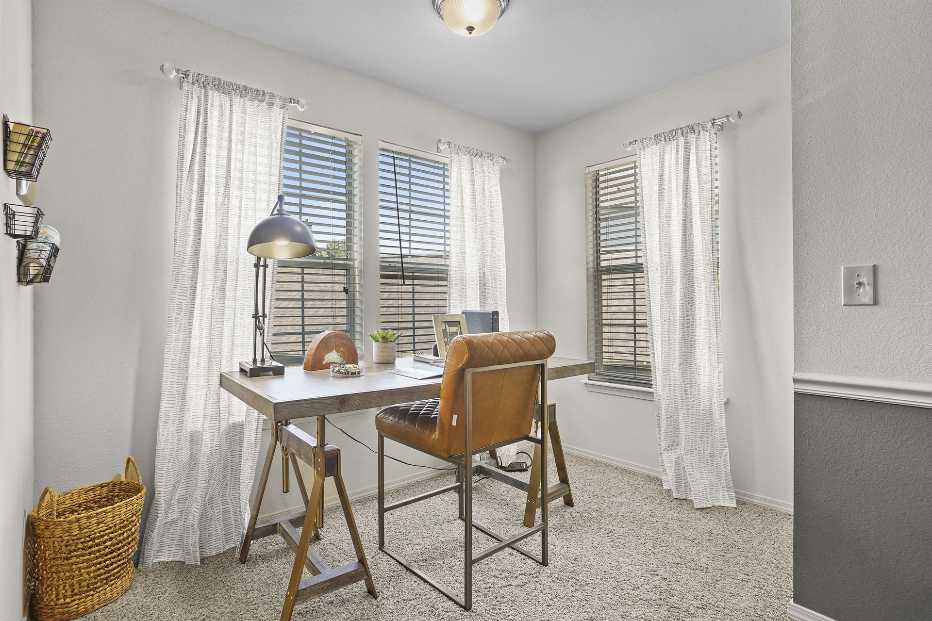Small apartment office with a wooden desk, leather chair, and three windows.