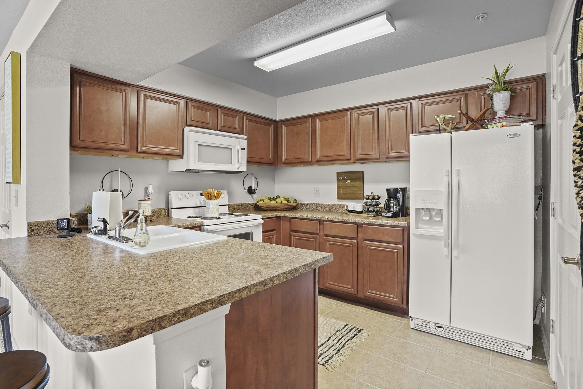 Apartment kitchen with brown wood cabinets, white appliances, and granite countertops.