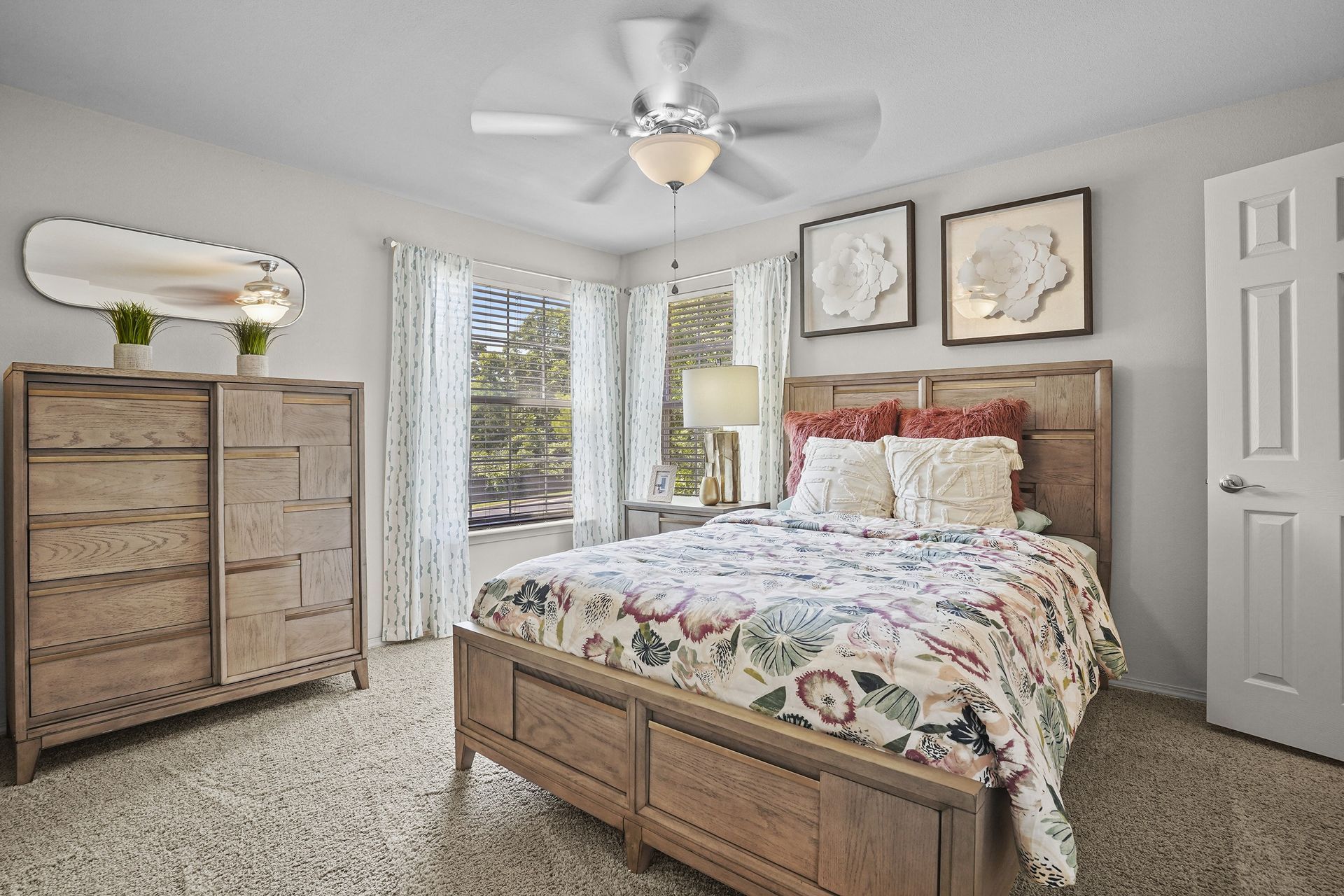 Bedroom with wooden furniture, bed with floral bedding, framed art, and a ceiling fan.