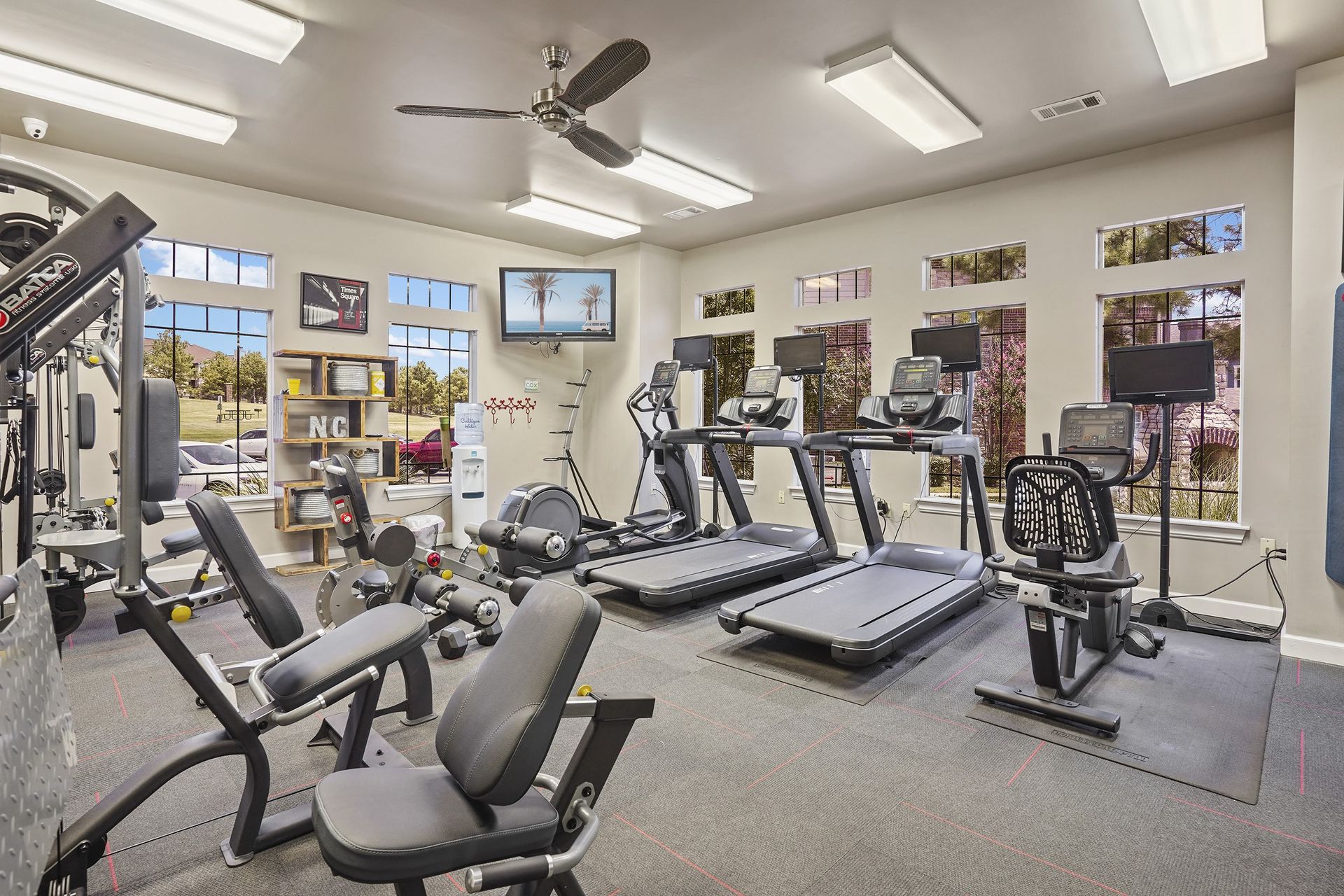 Gym with exercise equipment, windows, TV, and ceiling fan.
