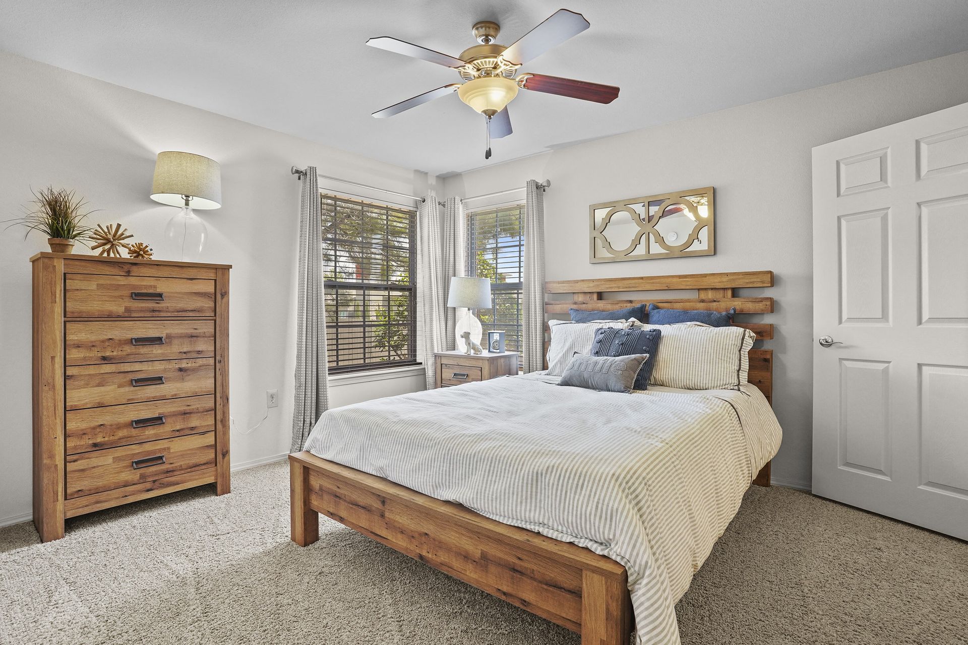 Furnished bedroom with wooden bed frame, matching dresser, nightstand, and two windows.