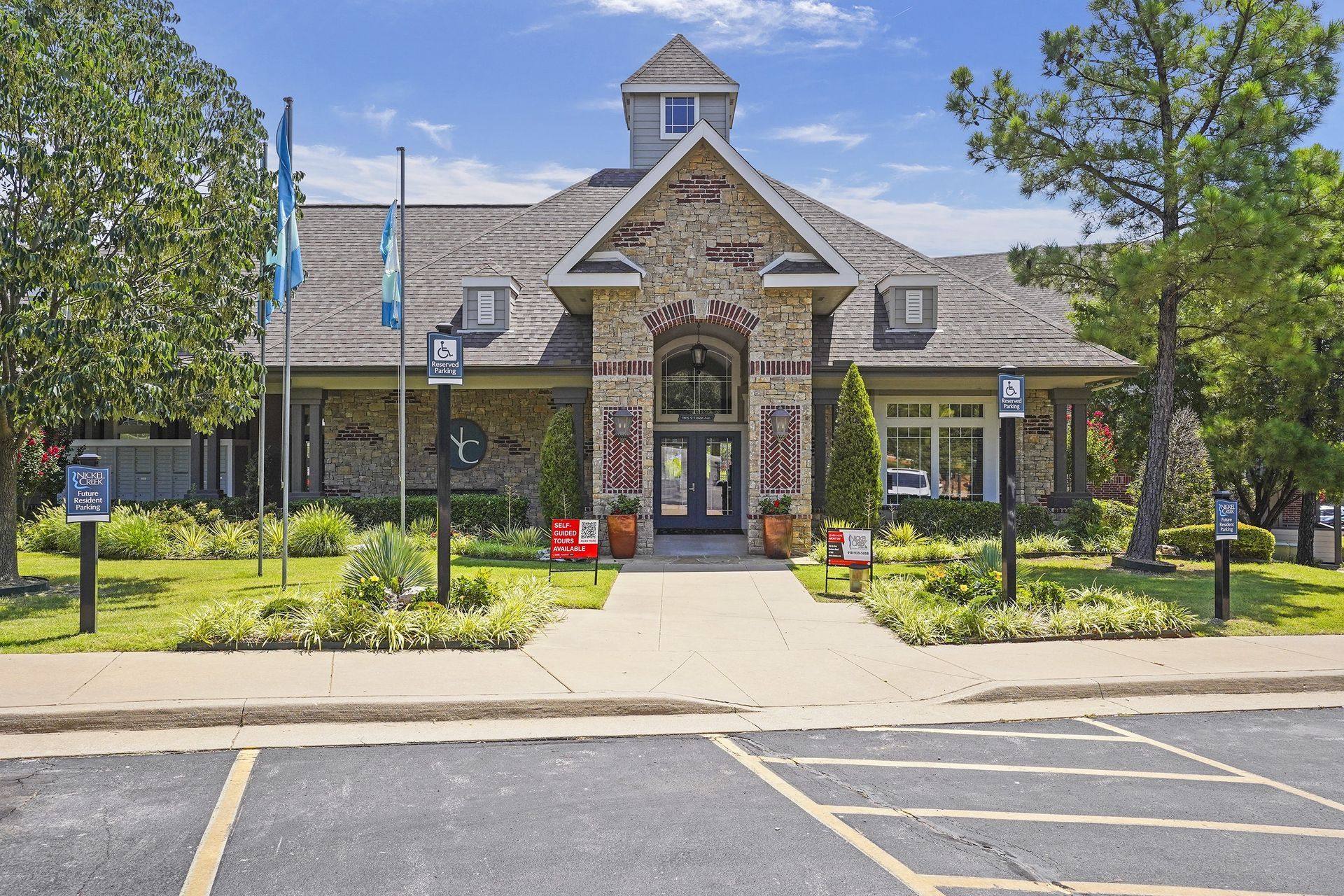 Stone building with a peaked roof, arched entrance, and flags, likely an apartment clubhouse.