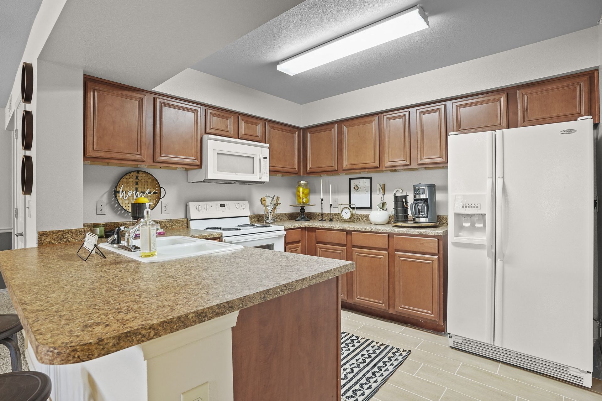 Kitchen in an apartment with brown wooden cabinets, white appliances, and a granite countertop island.