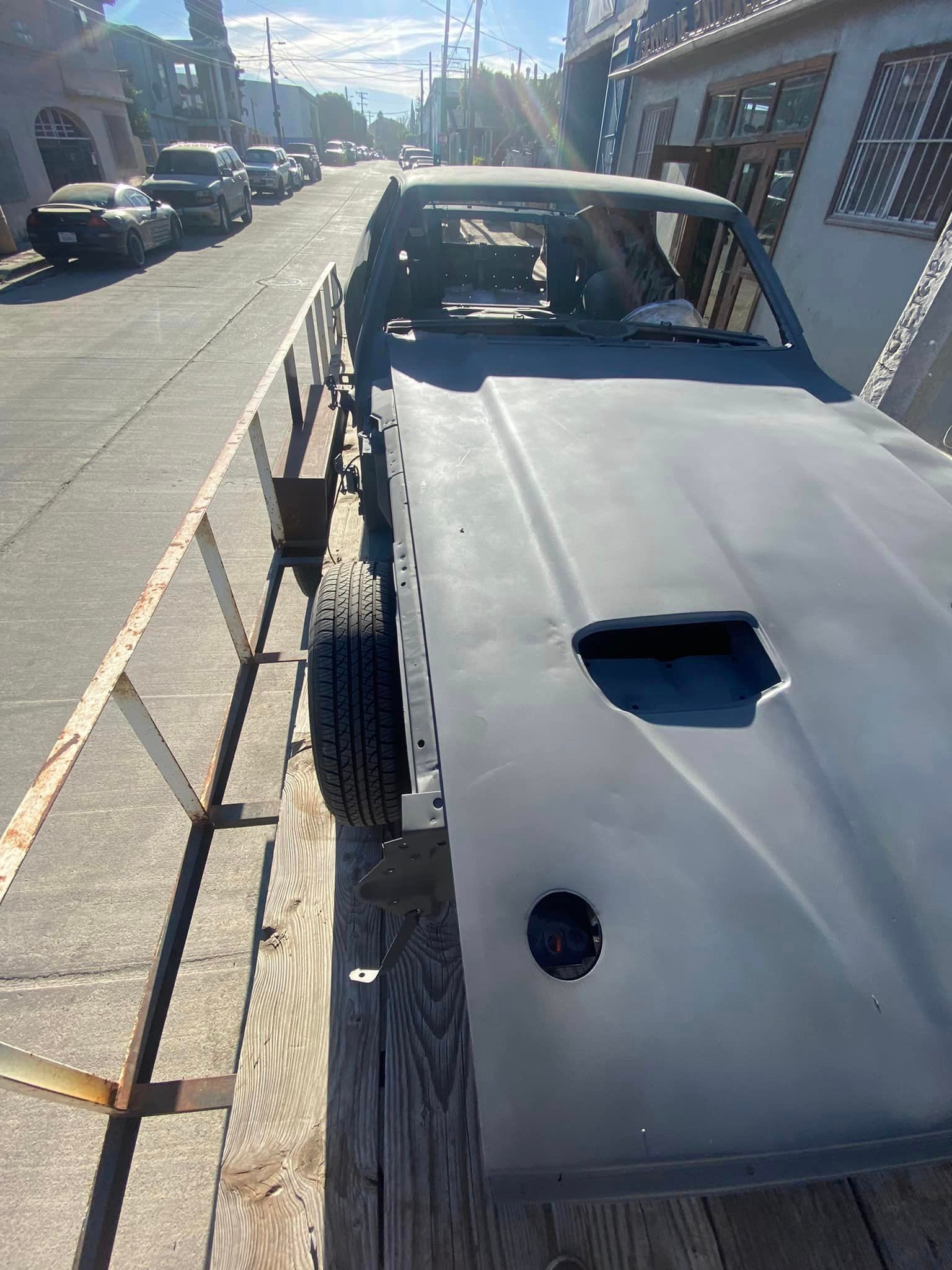 Un automóvil está sentado sobre un remolque al costado de la carretera.