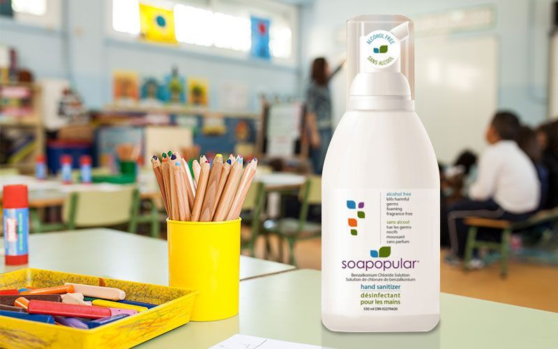 Soap bottle on a desk in a classroom, next to pencils and crayons.