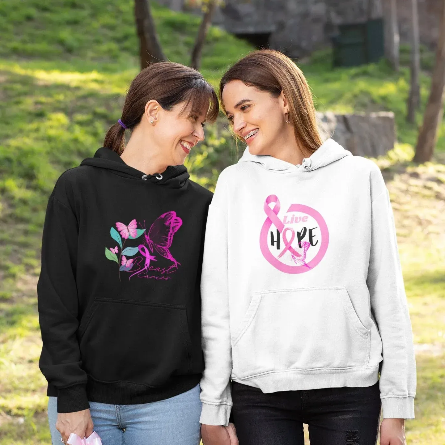 Two women wearing breast cancer awareness hoodies, smiling outside.