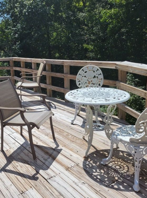 Outdoor deck with a white wrought iron table and chairs, plus two other chairs.