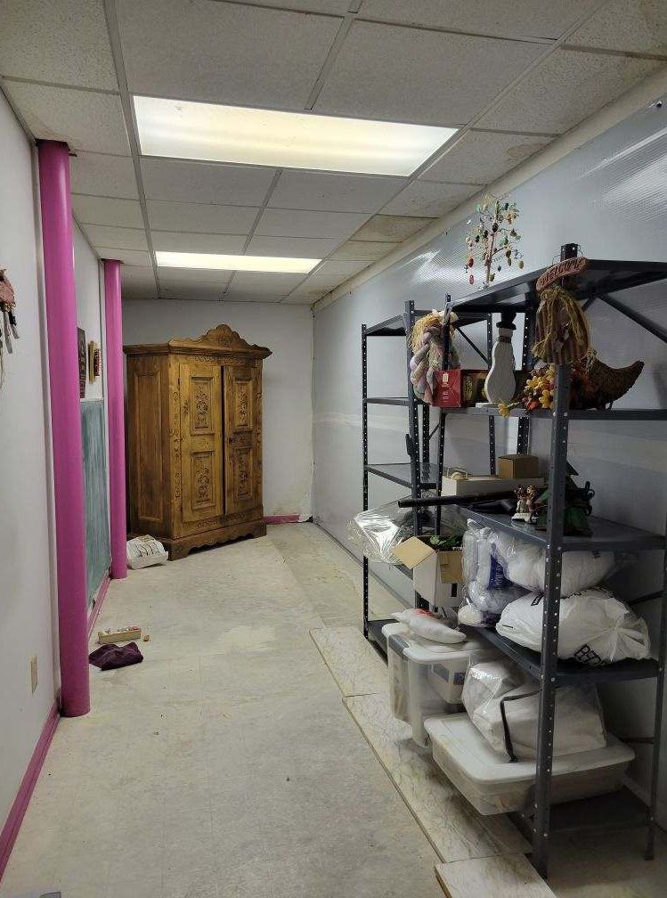 Narrow room with storage shelves and a wooden cabinet. Pink pillars and fluorescent lighting.