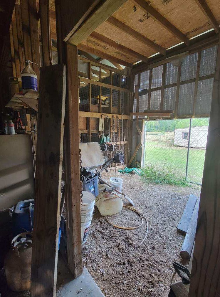 Interior view of a shed. Muddy floor, tools and supplies scattered. Open doorway leads to grassy field.