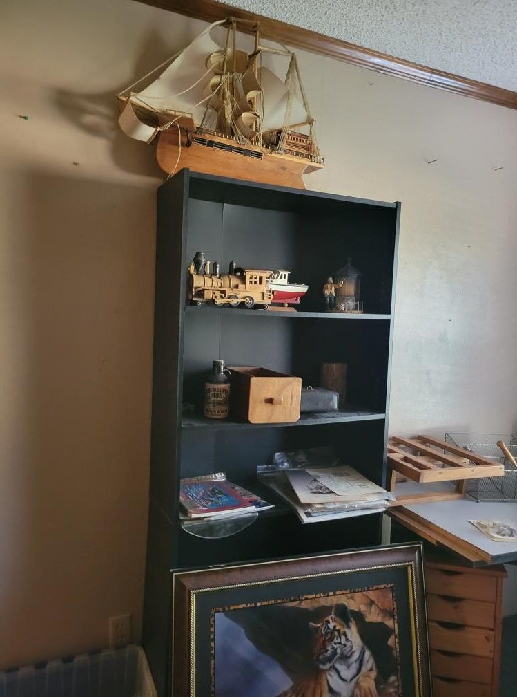 Black bookshelf with model ship, train, and other items. A framed picture rests in front.