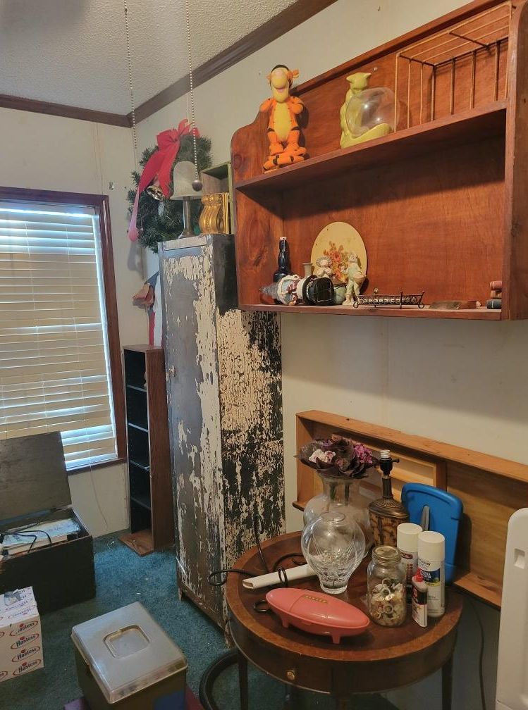 Room with shelves, a rusty cabinet, and a round table filled with objects. A Tigger figure sits on a shelf.
