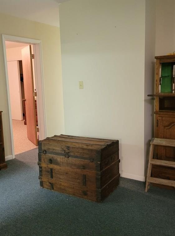 Antique wooden trunk on a blue carpet, next to a white wall and a doorway.